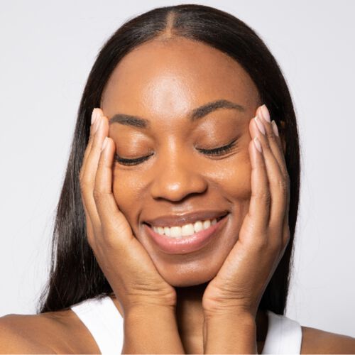 Mulher de pele negra sorrindo e colocando as mãos no rosto.